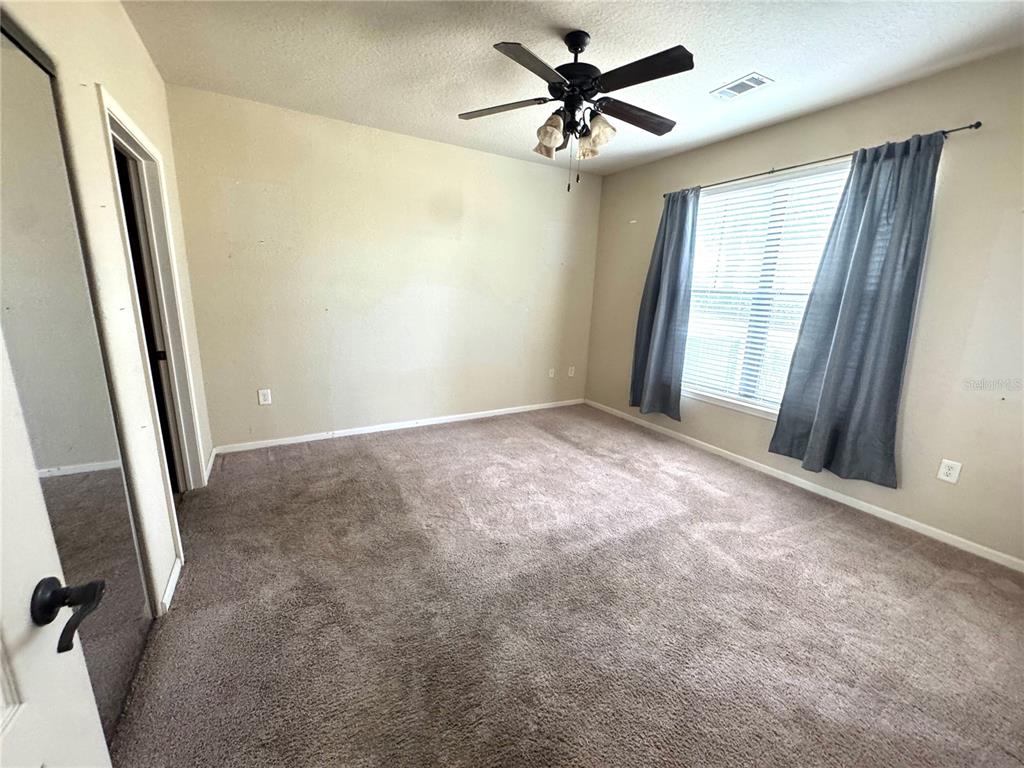 An empty bedroom features beige carpet, tan walls, a ceiling fan, and gray window curtains — 909 CHARO PARKWAY UNIT 1016, DAVENPORT, FL