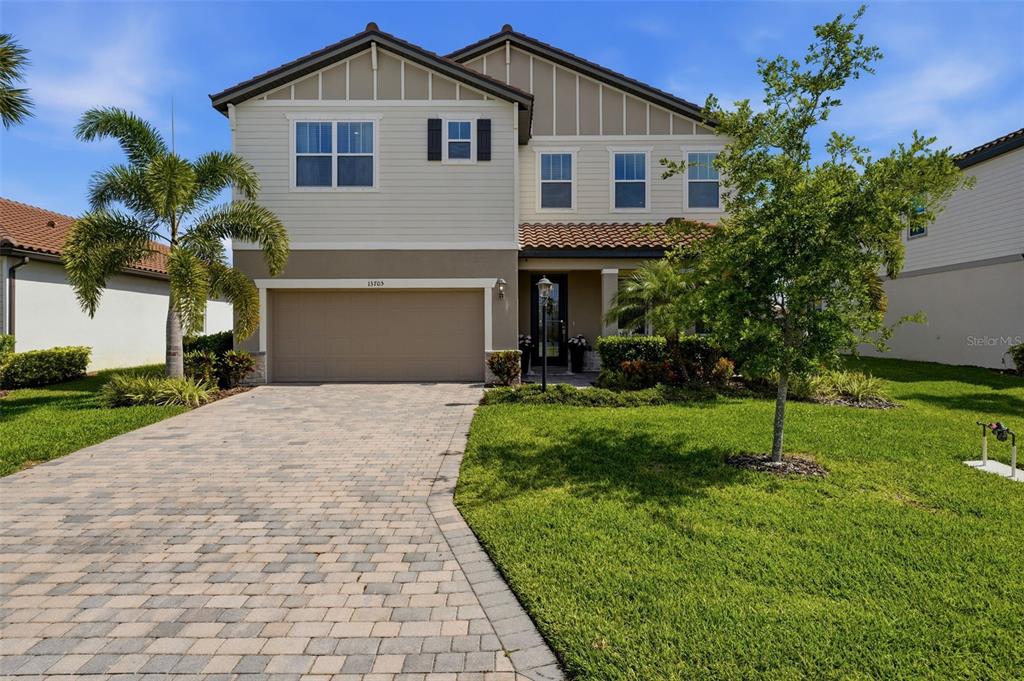A two-story suburban house features a tan exterior, a paved driveway, and a front lawn — 13705 FLAT WOODS TERRACE, BRADENTON, FL