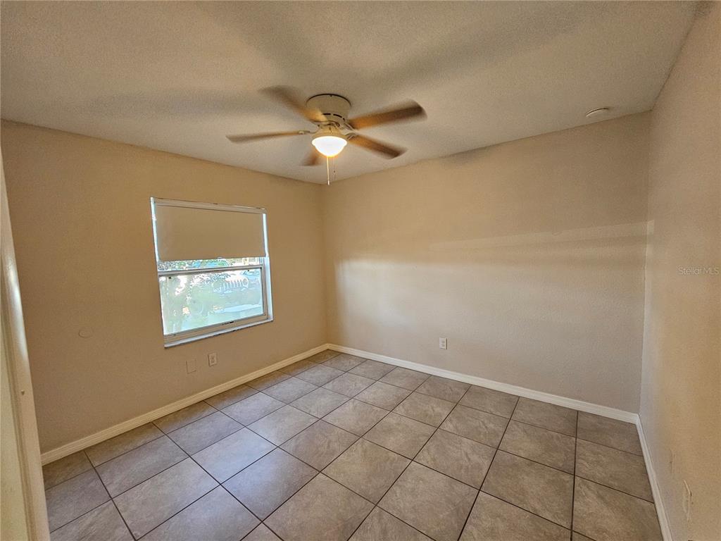 An empty bedroom features beige walls, a ceiling fan, and light-colored tile flooring — 8200 FAIRWAYS CIRCLE UNIT B102, OCALA, FL