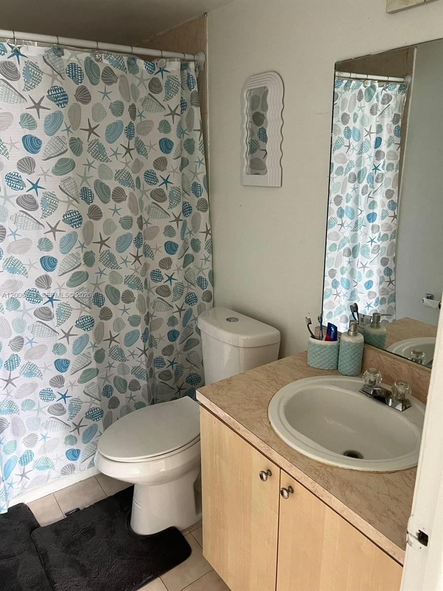 A bathroom features a seashell-patterned shower curtain, a white toilet, and a vanity with sink — 7125 NW 186th St # B502, Hialeah FL 33015, HIALEAH, FL