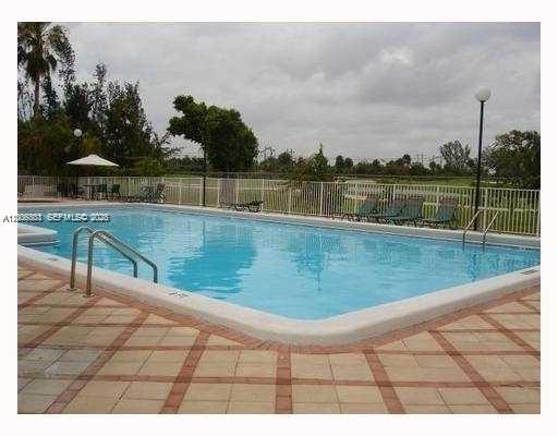 An outdoor swimming pool with a tiled deck and lounge chairs surrounded by a fence — 7125 NW 186th St # B502, Hialeah FL 33015, HIALEAH, FL