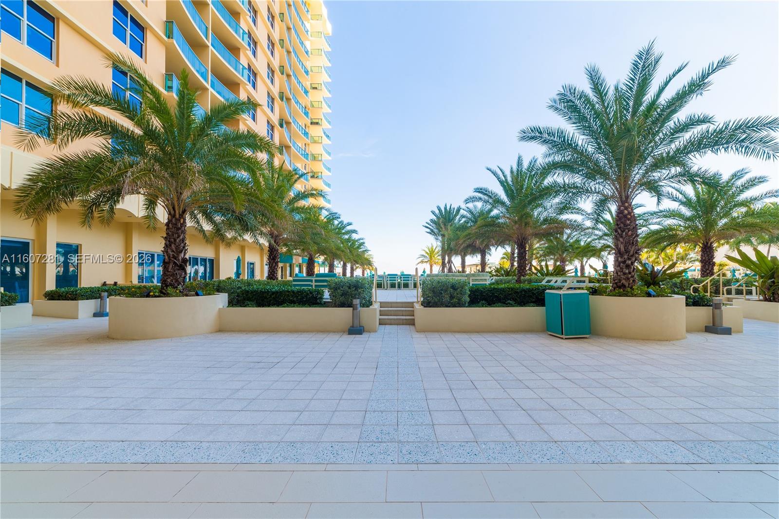 A paved outdoor patio features palm trees, low planters, and a view toward the ocean — 2501 S Ocean Dr # 303, Hollywood FL 33019, HOLLYWOOD, FL