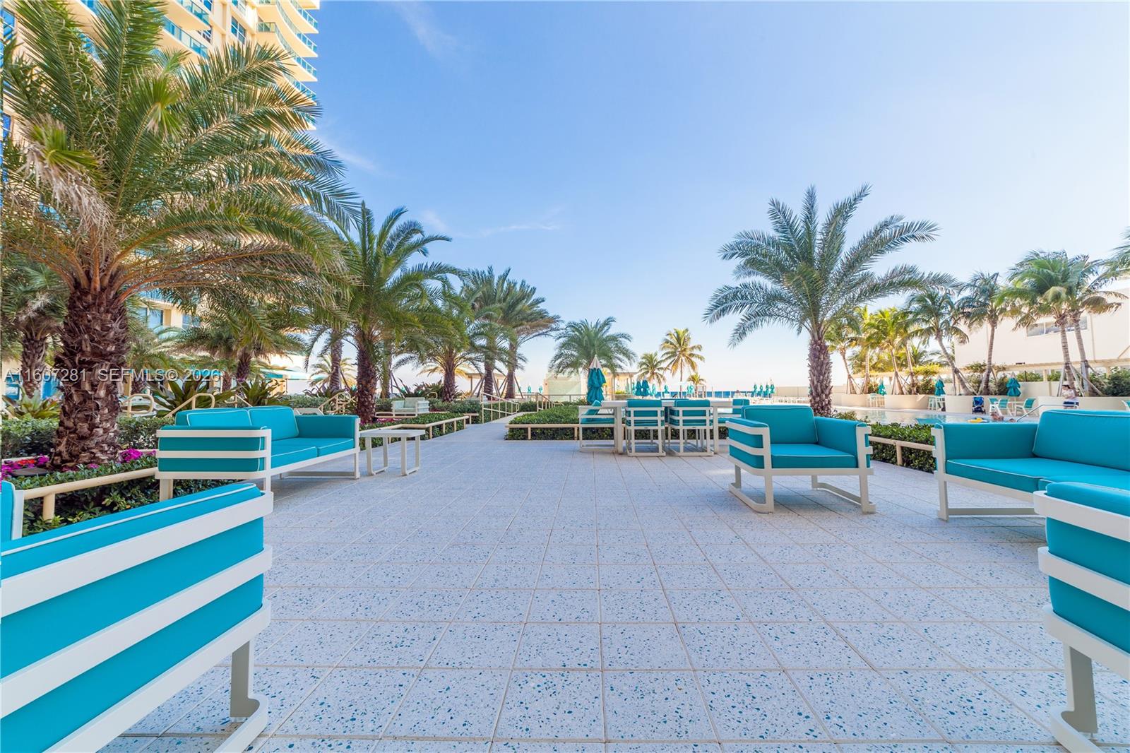 An outdoor patio features blue cushioned seating and palm trees near a swimming pool — 2501 S Ocean Dr # 303, Hollywood FL 33019, HOLLYWOOD, FL