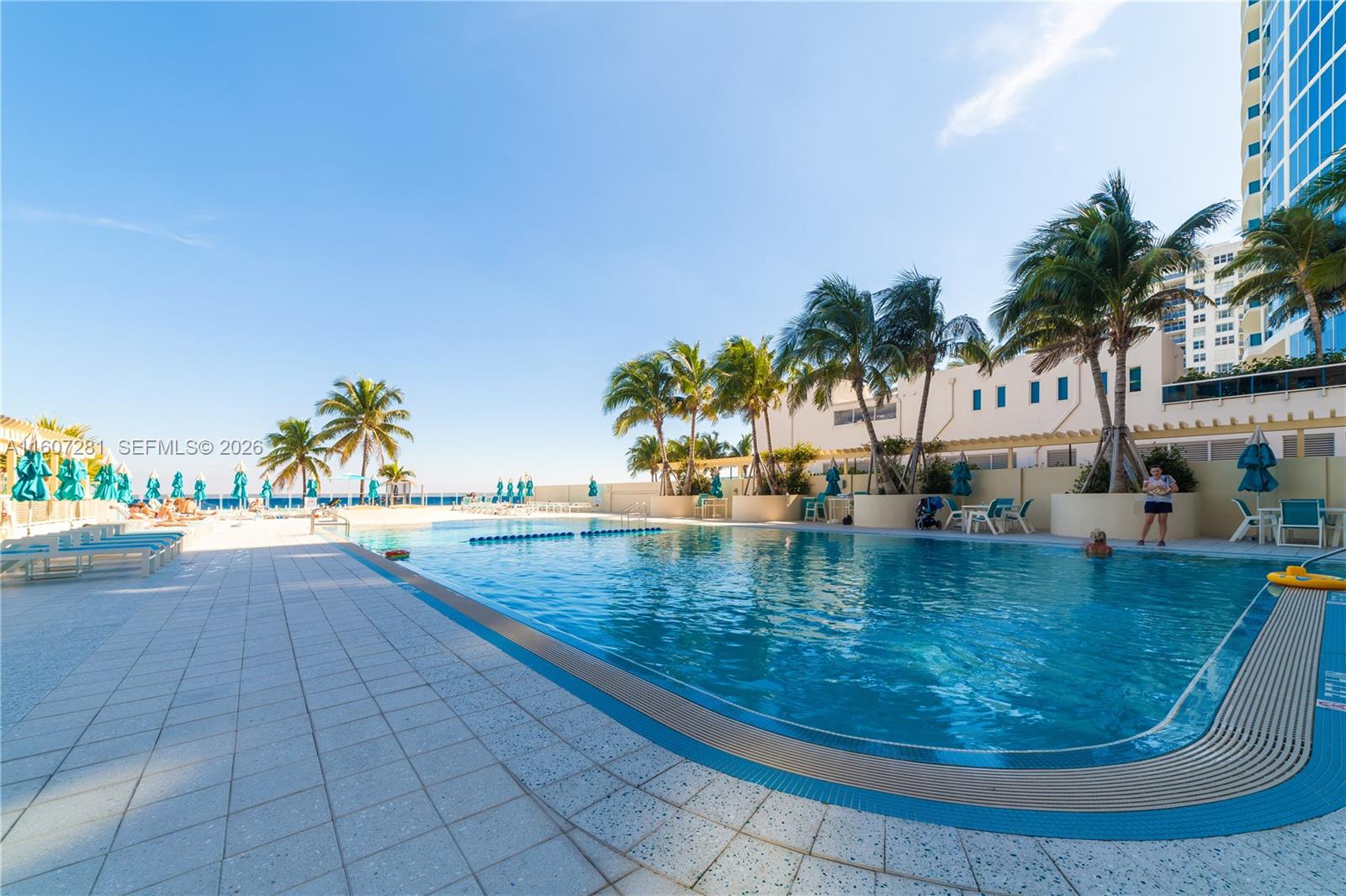 An outdoor swimming pool is surrounded by a tiled deck, palm trees, and lounge chairs — 2501 S Ocean Dr # 303, Hollywood FL 33019, HOLLYWOOD, FL