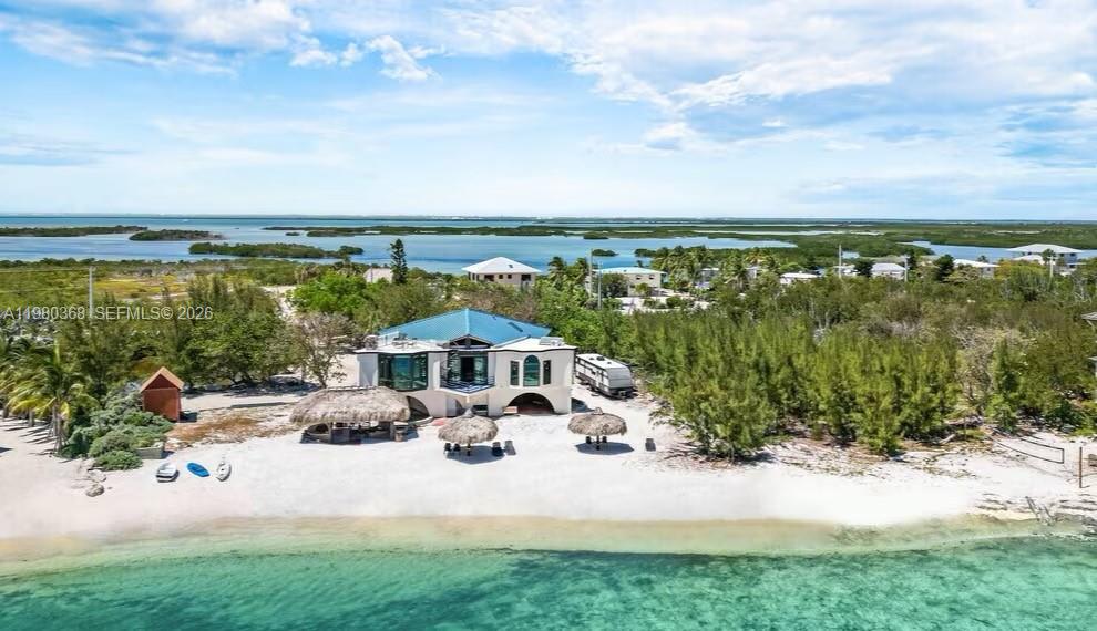 An aerial view shows a white house with a blue roof situated on a sandy beach — 1557 Long Beach Dr, Big Pine FL 33043, BIG PINE, FL