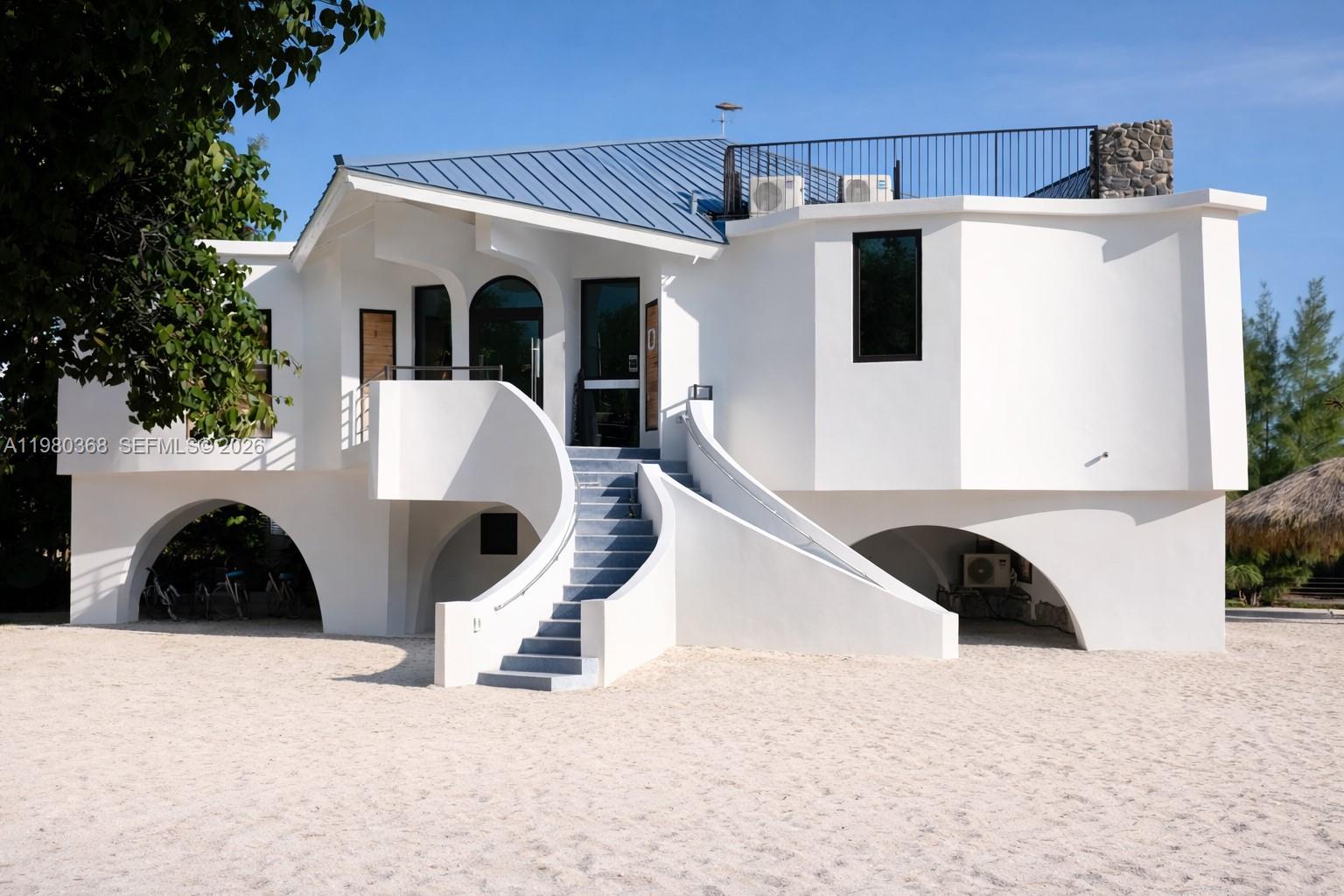 A white two-story beach house features a curved staircase leading to the main entrance — 1557 Long Beach Dr, Big Pine FL 33043, BIG PINE, FL