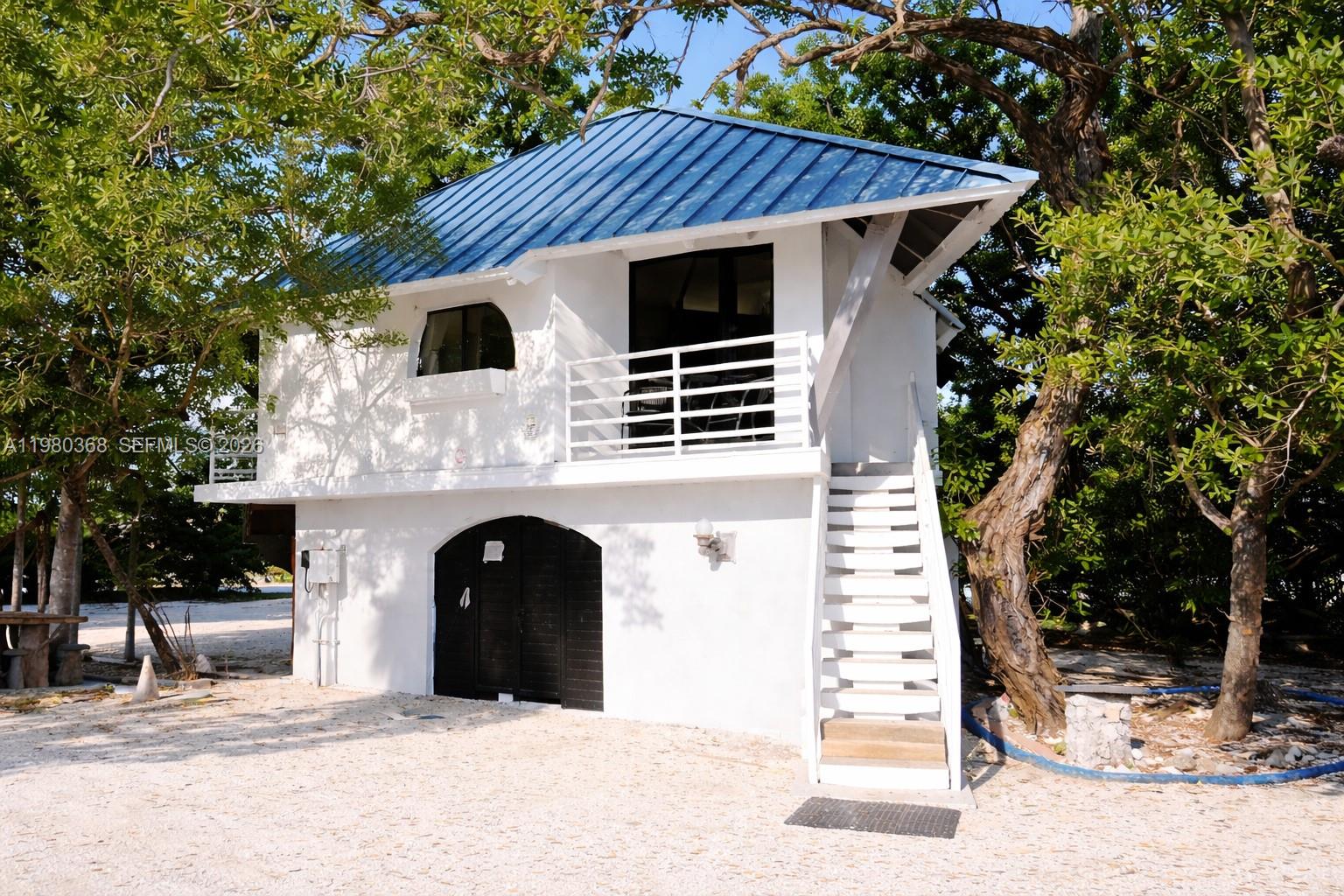 A two-story white building with a blue metal roof and an exterior staircase — 1557 Long Beach Dr, Big Pine FL 33043, BIG PINE, FL