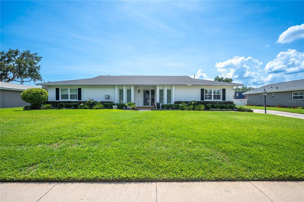 A single-story white house with a large green lawn under a bright blue sky — 1211 HUNT AVENUE, LAKELAND, FL