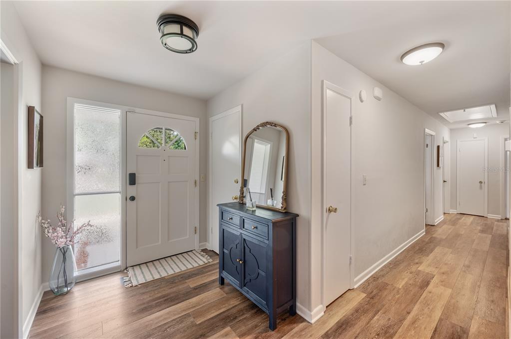 An entryway features wood-look flooring, a white front door with a sidelight, and a blue cabinet — 1211 HUNT AVENUE, LAKELAND, FL