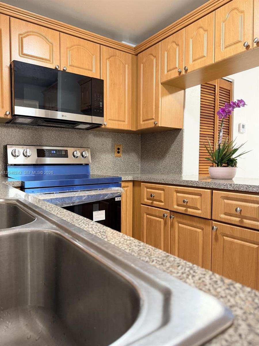 A kitchen features light wood cabinets, granite countertops, and a stainless steel oven and microwave — 1910 W 56th St # 3312, Hialeah FL 33012, HIALEAH, FL