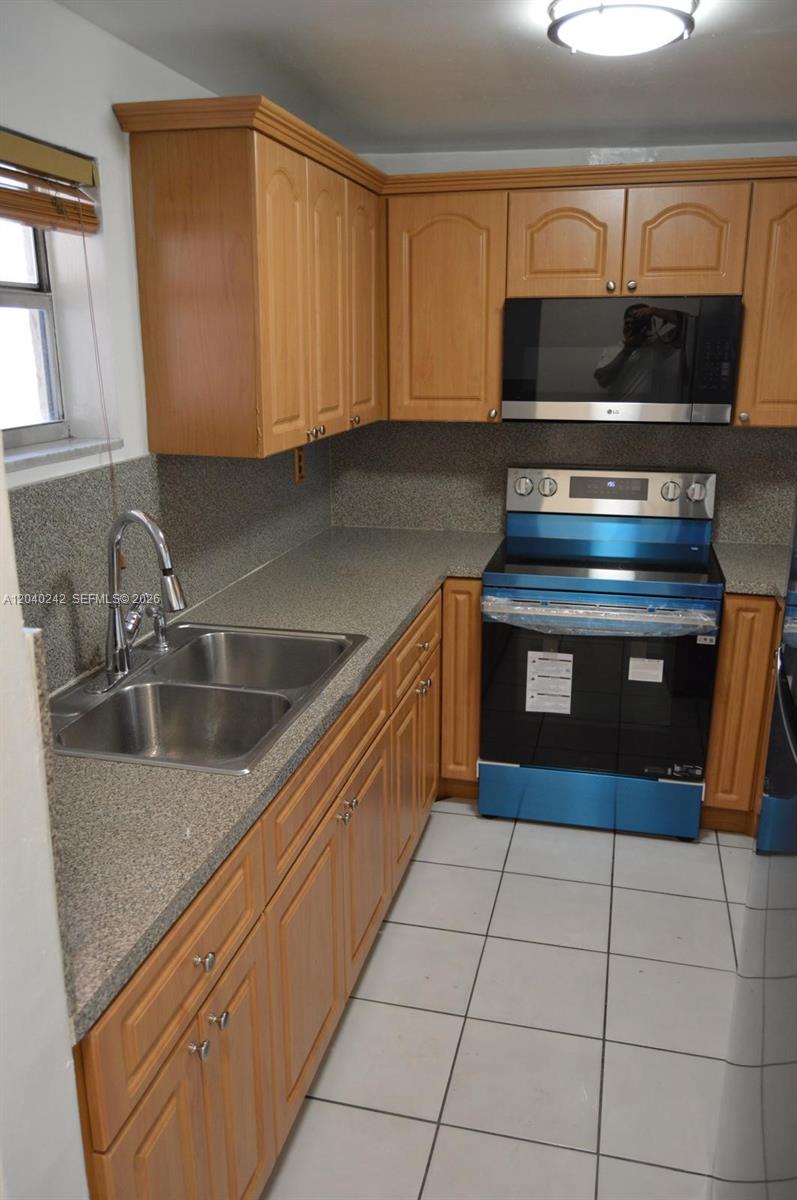A kitchen features light wood cabinets, speckled gray countertops, stainless steel appliances, and white tile flooring — 1910 W 56th St # 3312, Hialeah FL 33012, HIALEAH, FL
