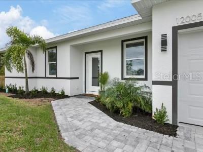 A white house exterior features a paved walkway, a palm tree, and dark window trim — 12005 HELICON AVENUE, PORT CHARLOTTE, FL