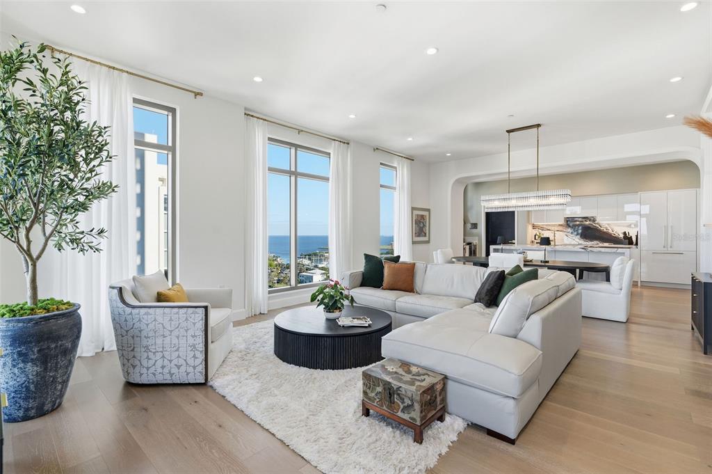 A modern living room with a white sectional, round coffee table, and ocean view windows — 126 4TH AVENUE NE UNIT 1401, ST PETERSBURG, FL