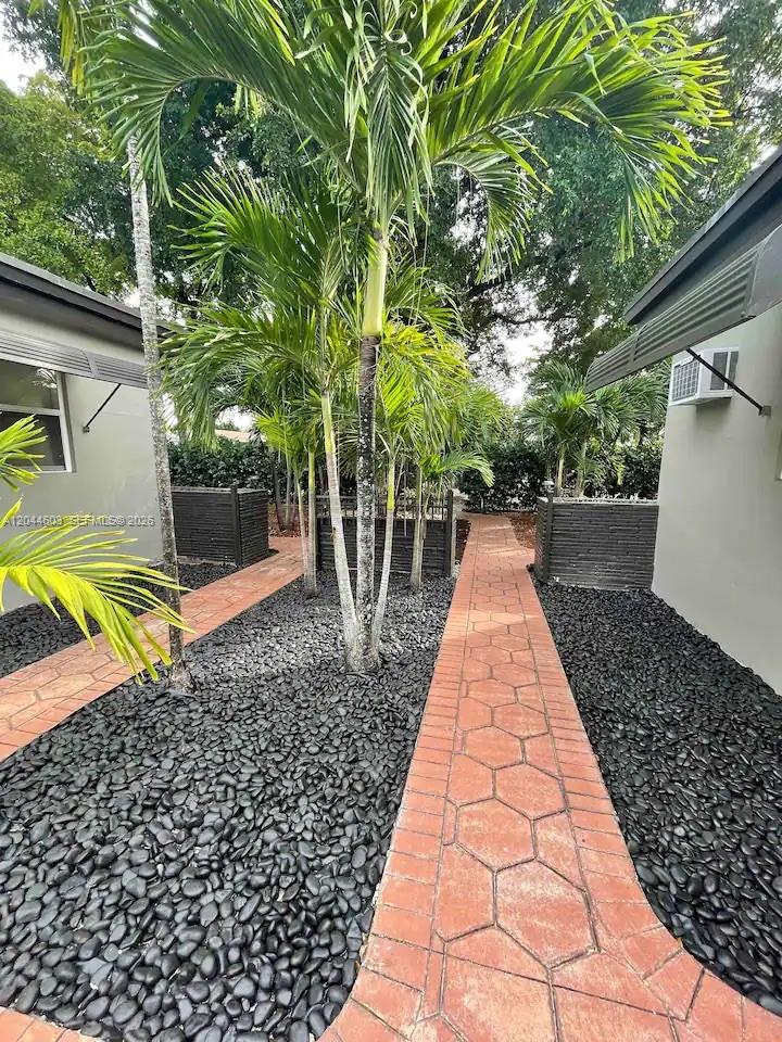 A paved walkway runs between two buildings through a garden with palm trees and gravel — 1925 Dewey St, Hollywood FL 33020, HOLLYWOOD, FL