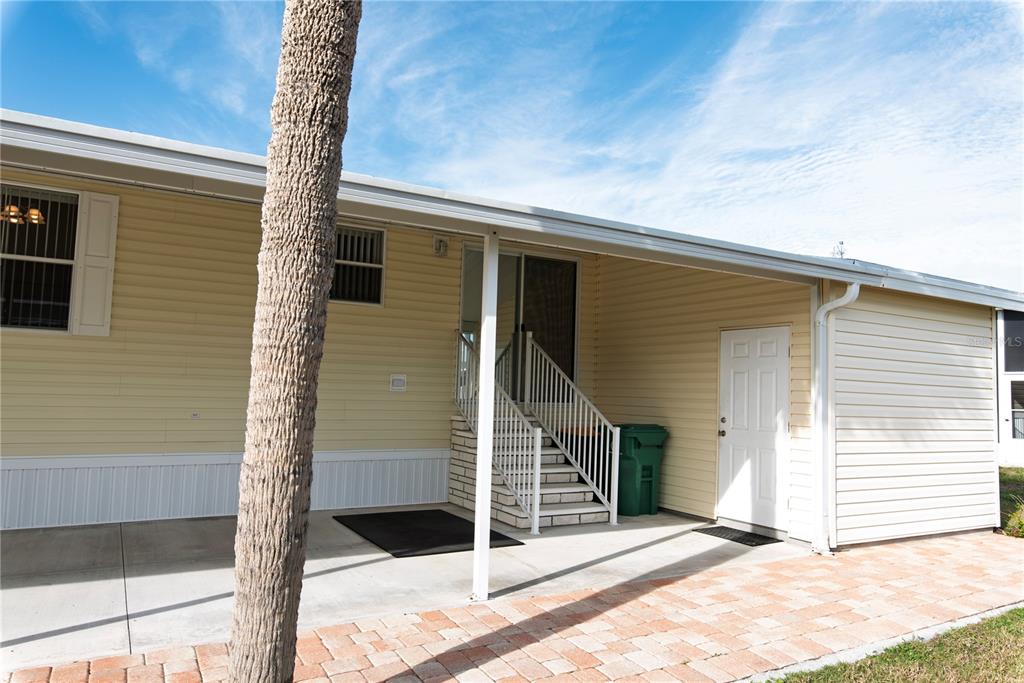 A pale yellow mobile home exterior features a concrete patio, stairs, and a white door — 33 AMSTERDAM AVENUE, PUNTA GORDA, FL
