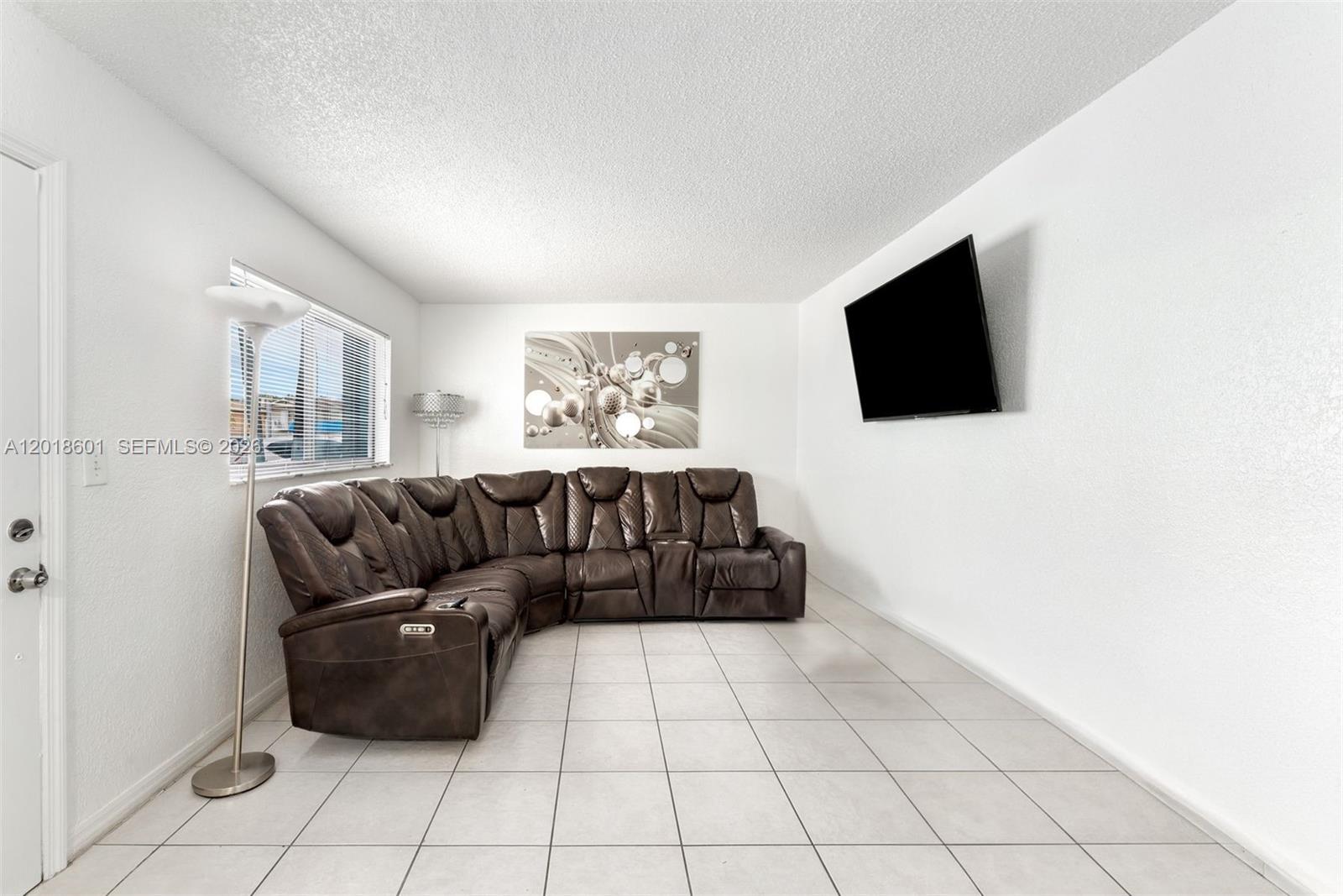 A living room features a brown sectional sofa, a wall-mounted television, and tiled flooring — 5706 W 26th Ave # 5706, Hialeah FL 33016, HIALEAH, FL