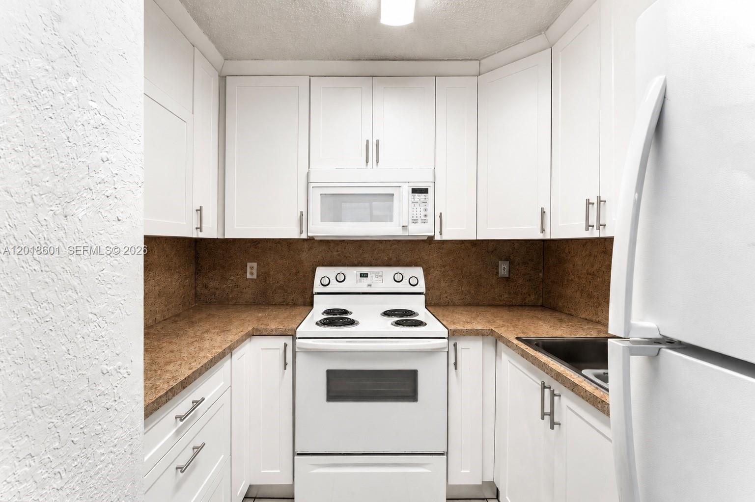 A small kitchen features white cabinets, a white stove, a microwave, and brown countertops — 5706 W 26th Ave # 5706, Hialeah FL 33016, HIALEAH, FL