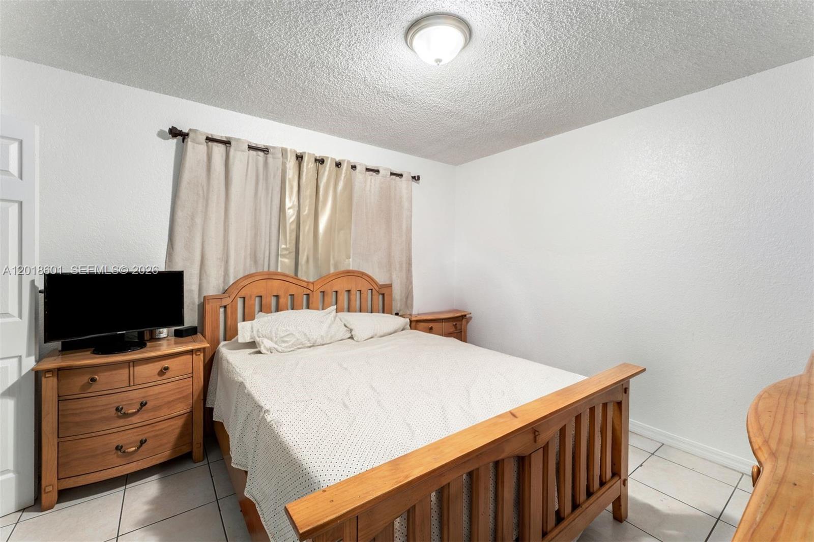 A bedroom features a wooden bed frame, a matching dresser with a television, and tile flooring — 5706 W 26th Ave # 5706, Hialeah FL 33016, HIALEAH, FL