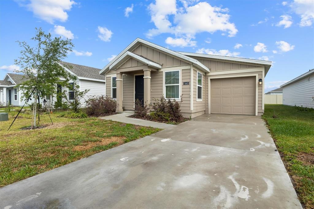 A single-story tan house with a front porch, garage, and concrete driveway under a blue sky — 1665 TEAGAN LANE, WINTER HAVEN, FL