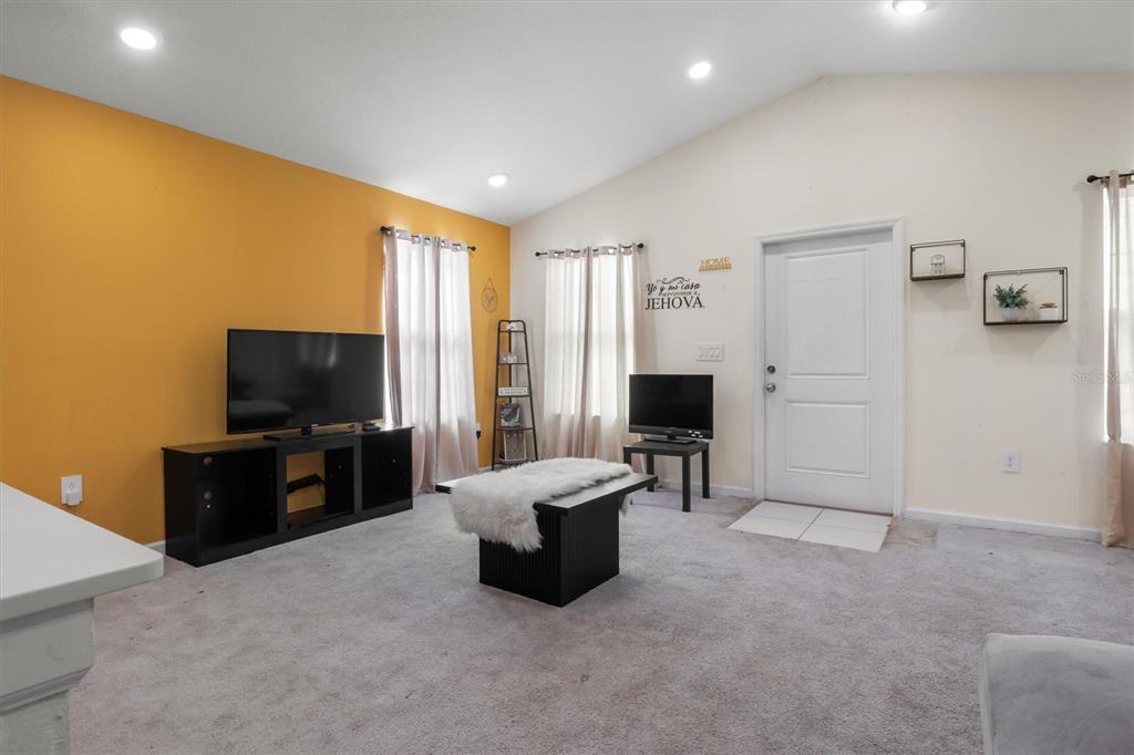 A living room features a yellow accent wall, carpeted flooring, and a vaulted ceiling — 1665 TEAGAN LANE, WINTER HAVEN, FL