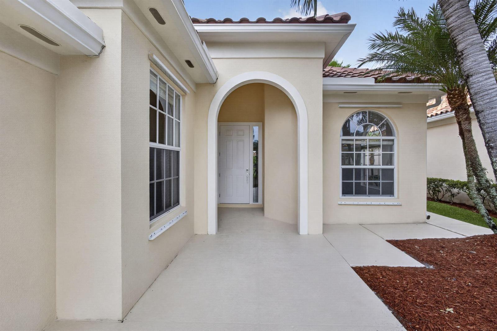 The exterior of a beige house features an arched entryway, a white door, and windows — 2625 Kittbuck Way, West Palm Beach FL 33411, WEST PALM BEACH, FL