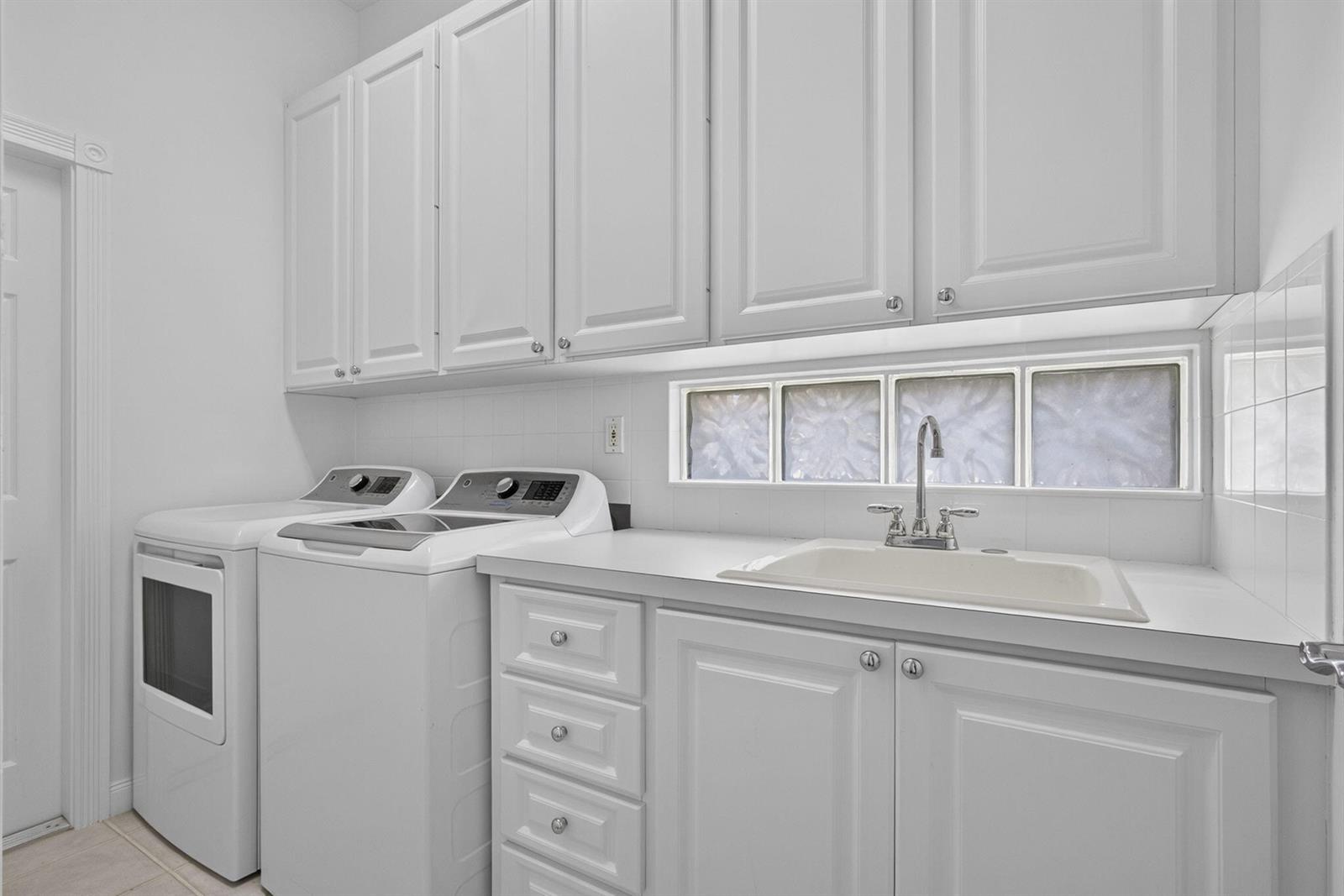A laundry room features white cabinets, a utility sink, and a washer and dryer set — 2625 Kittbuck Way, West Palm Beach FL 33411, WEST PALM BEACH, FL