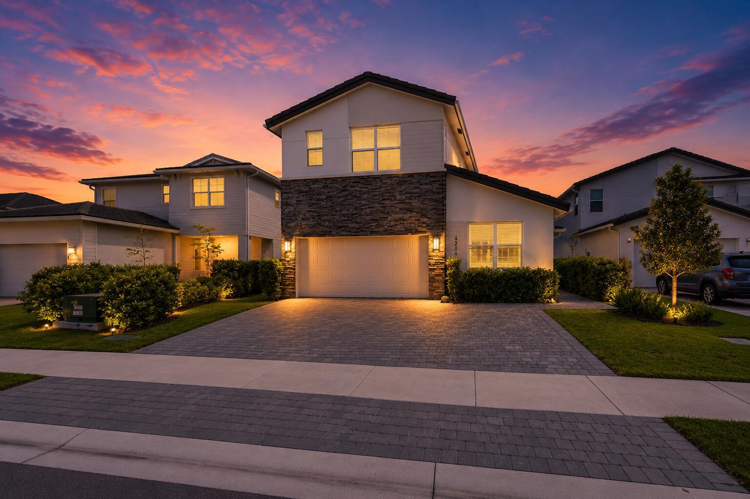 A two-story suburban house with a stone facade, paved driveway, and sunset sky — 4206 Rosa Drive, Deerfield Beach FL 33064, DEERFIELD BEACH, FL