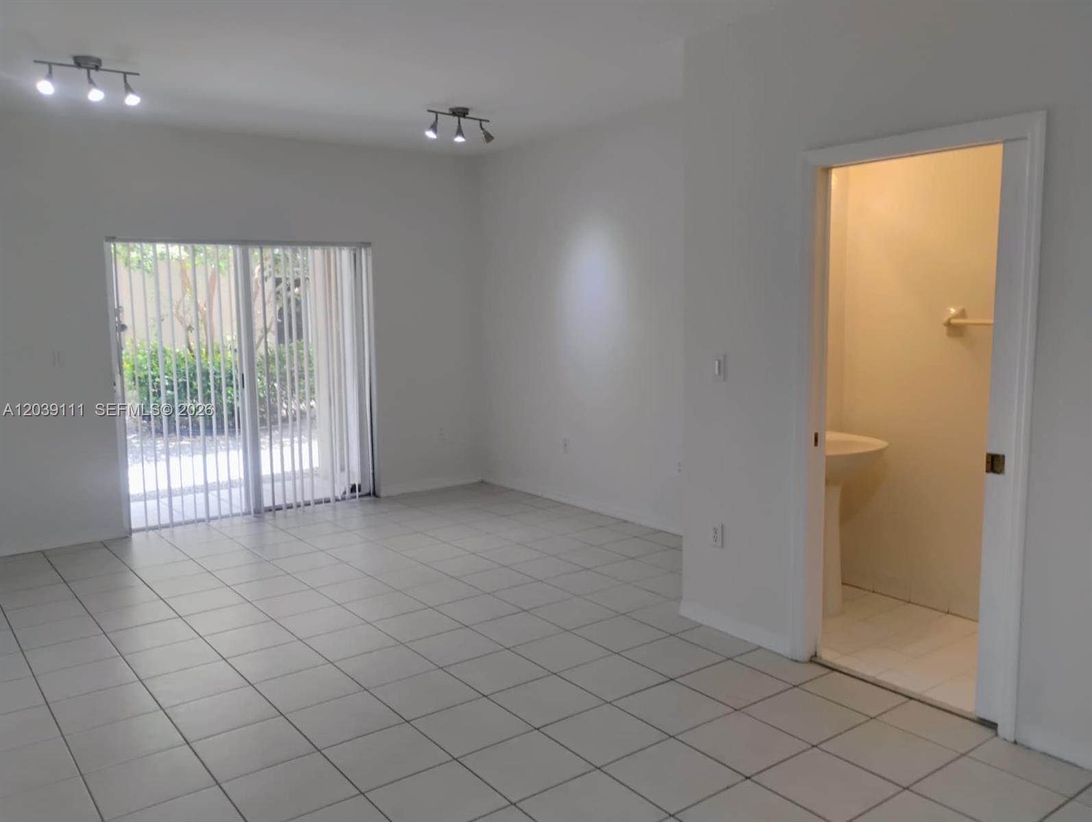 A room with white tile floors, two ceiling lights, sliding glass doors, and an attached bathroom — 5725 NW 114th Path # 107, Doral FL 33178, DORAL, FL