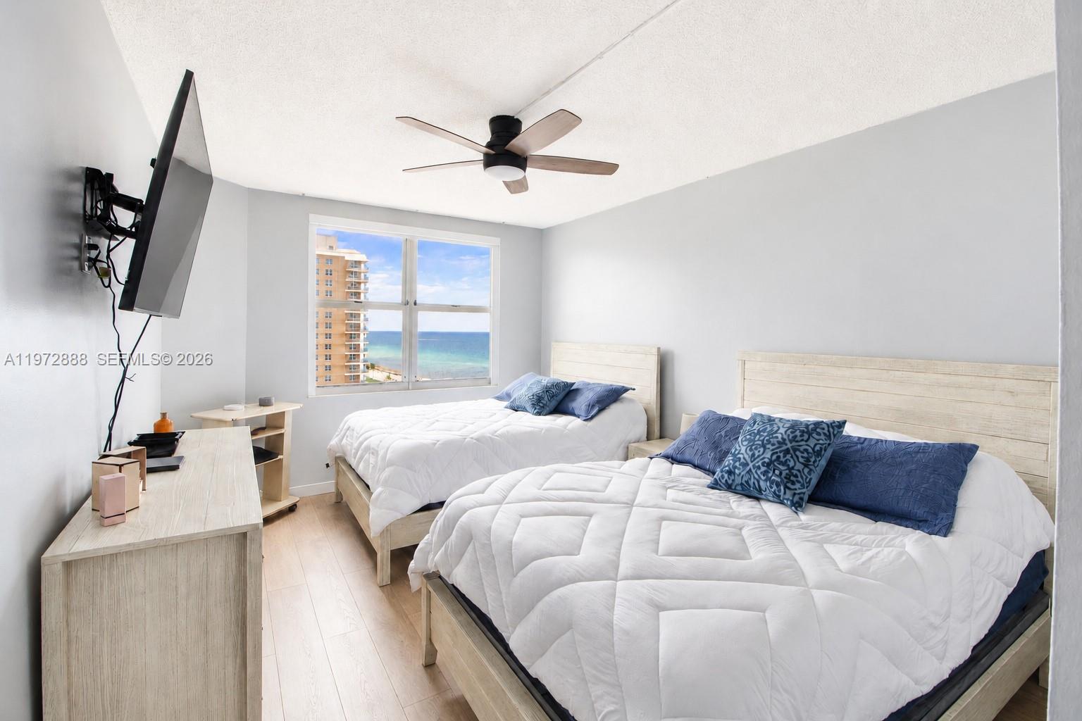 A bedroom features two beds, a dresser, a wall-mounted television, and an ocean view — 1950 S Ocean Dr # 11D, Hallandale Beach FL 33009, HALLANDALE BEACH, FL