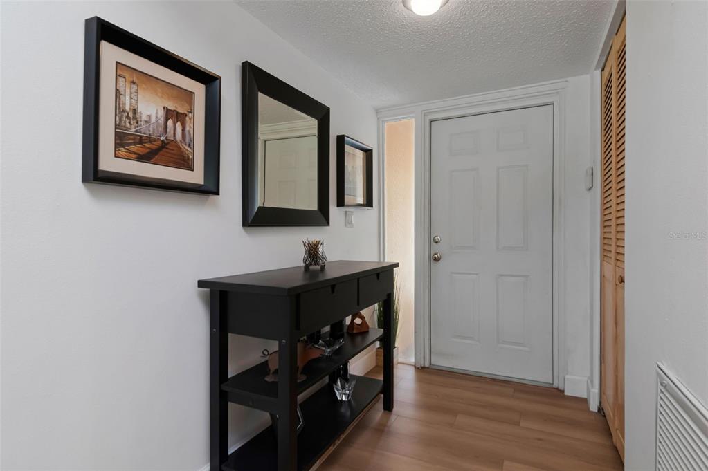 An entryway features a black console table, a mirror, wall art, and wood-look flooring — 1150 BROOK DRIVE W, DUNEDIN, FL