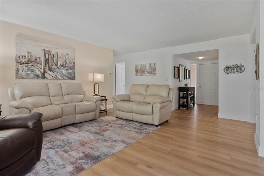 A living room features light-colored sofas, a patterned area rug, and light wood-look flooring — 1150 BROOK DRIVE W, DUNEDIN, FL