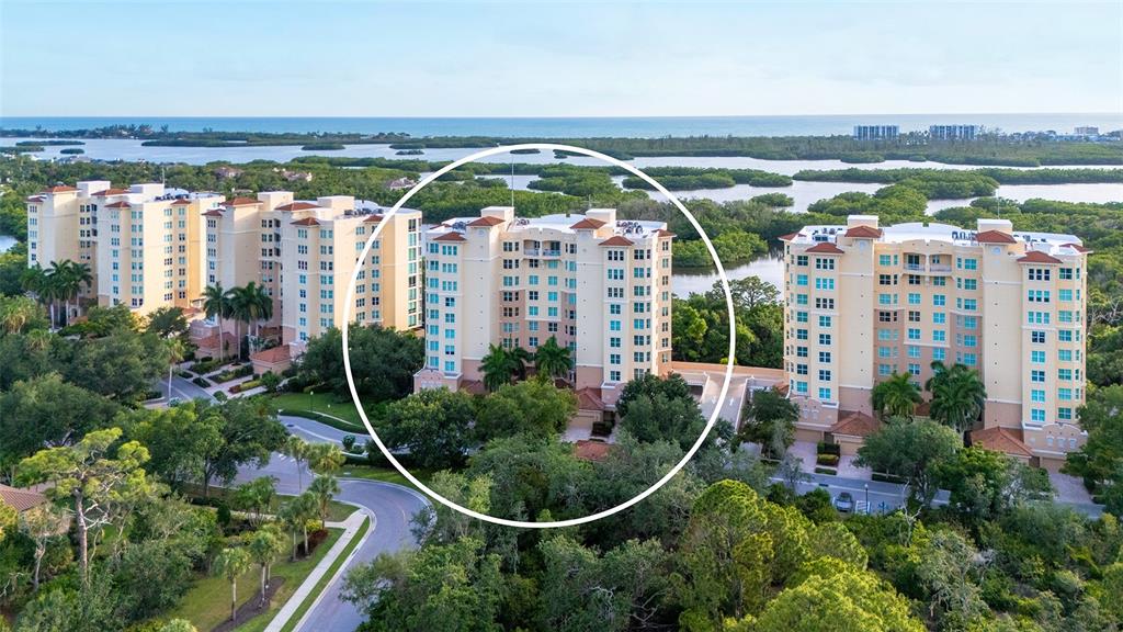 An aerial view shows three multi-story residential buildings surrounded by lush greenery and water — 401 N POINT ROAD UNIT 504, OSPREY, FL