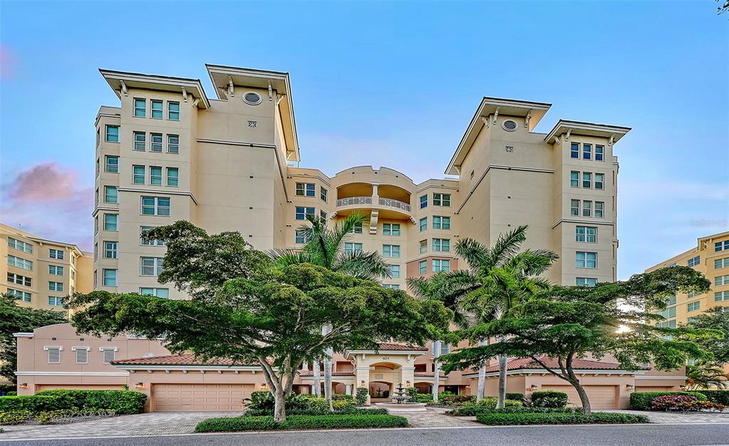 A multi-story beige apartment building features a central courtyard, arched entrance, and surrounding palm trees — 401 N POINT ROAD UNIT 504, OSPREY, FL