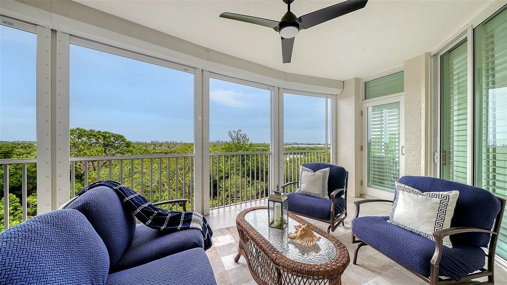 A screened-in balcony features blue patio furniture, a wicker coffee table, and a ceiling fan — 401 N POINT ROAD UNIT 504, OSPREY, FL