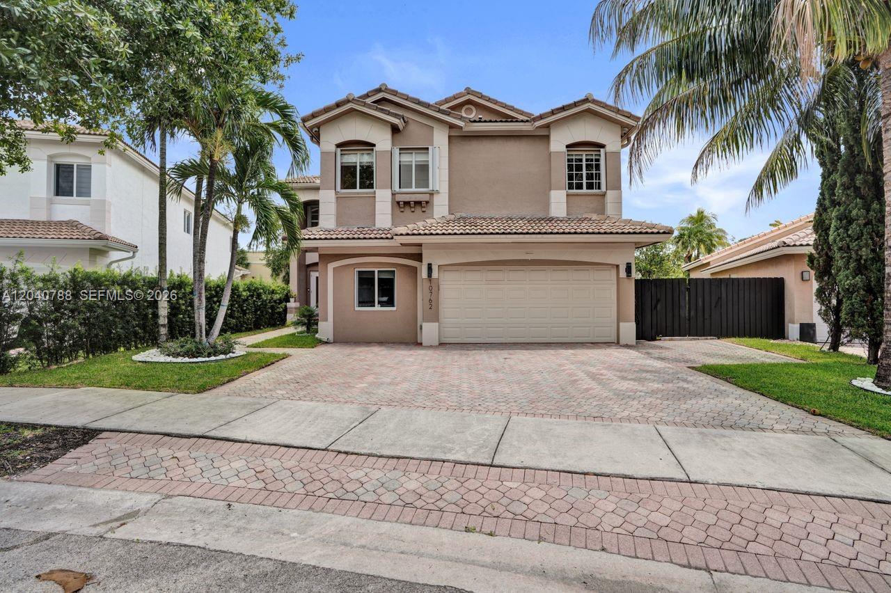 A two-story suburban house features a beige stucco exterior, a tiled roof, and a driveway — 10762 NW 71st St, Doral FL 33178, DORAL, FL