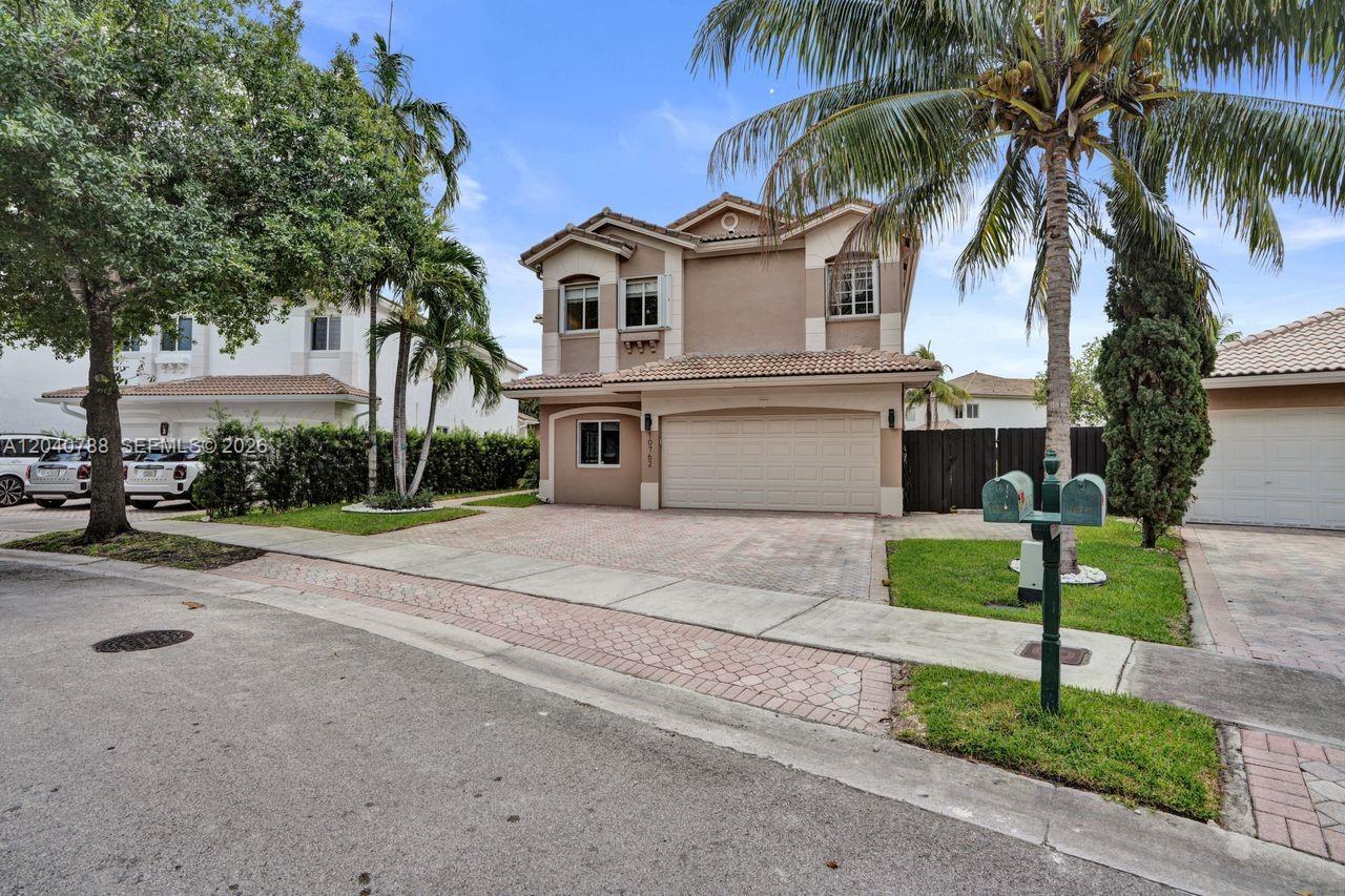 A two-story suburban house features a tan stucco exterior, a paved driveway, and palm trees — 10762 NW 71st St, Doral FL 33178, DORAL, FL