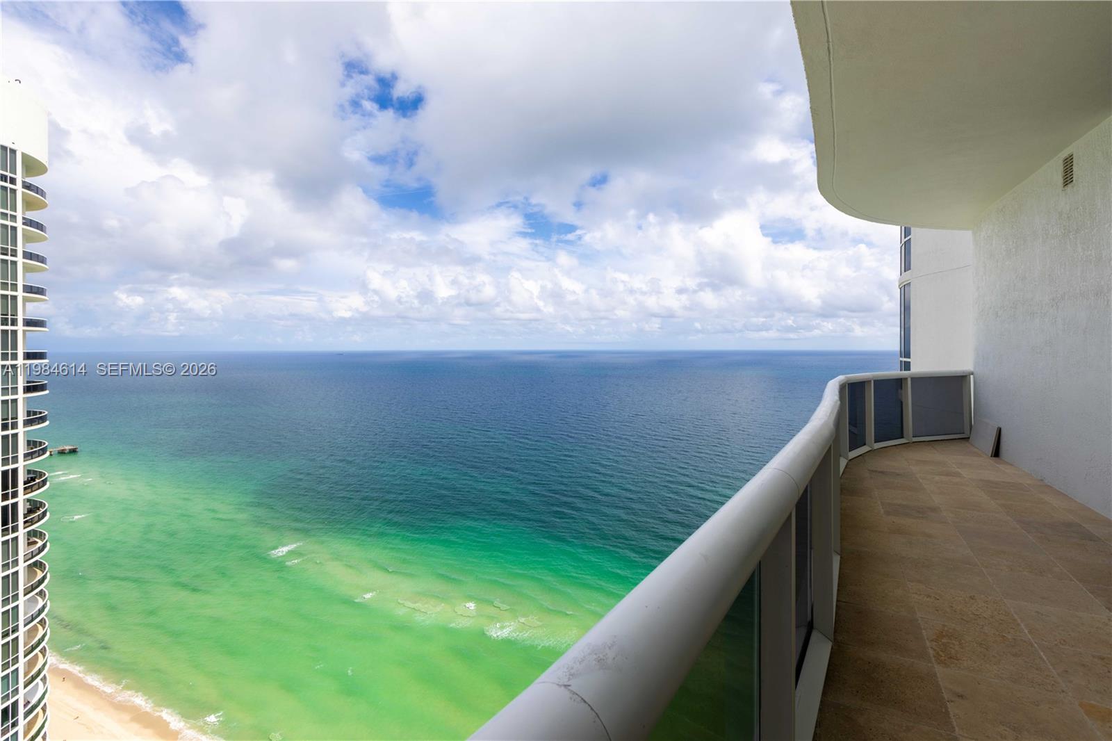 A high-rise balcony overlooks the ocean with a view of a neighboring building — SUNNY ISLES BEACH, FL