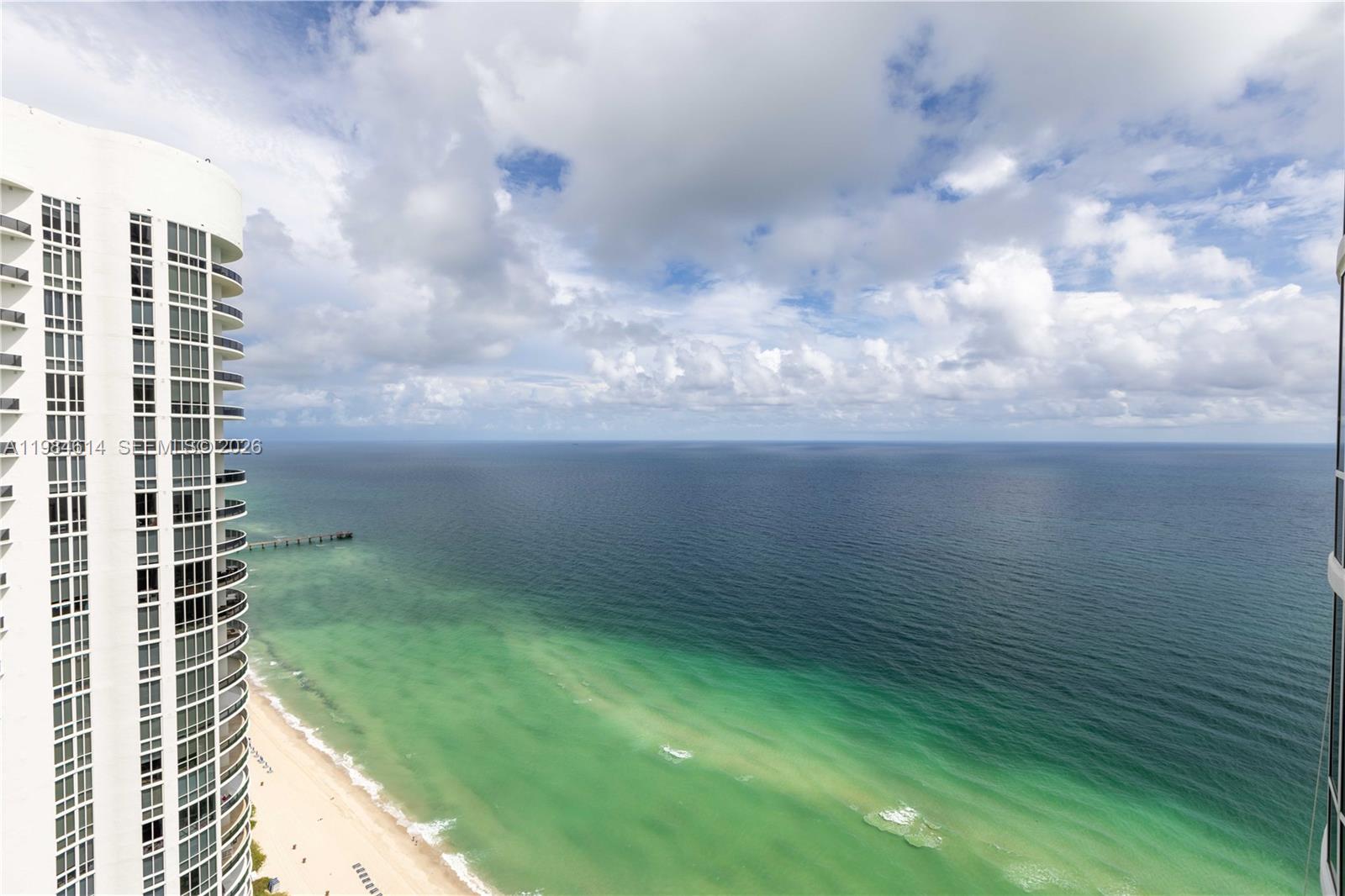 A high-angle view shows a tall residential building overlooking a sandy beach and ocean — SUNNY ISLES BEACH, FL