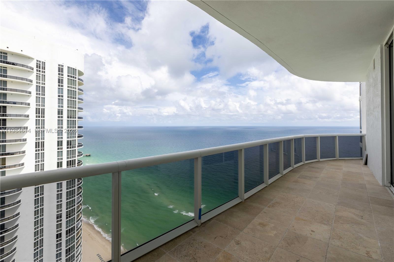 A high-rise balcony with tiled flooring overlooks the ocean and a neighboring residential tower — SUNNY ISLES BEACH, FL