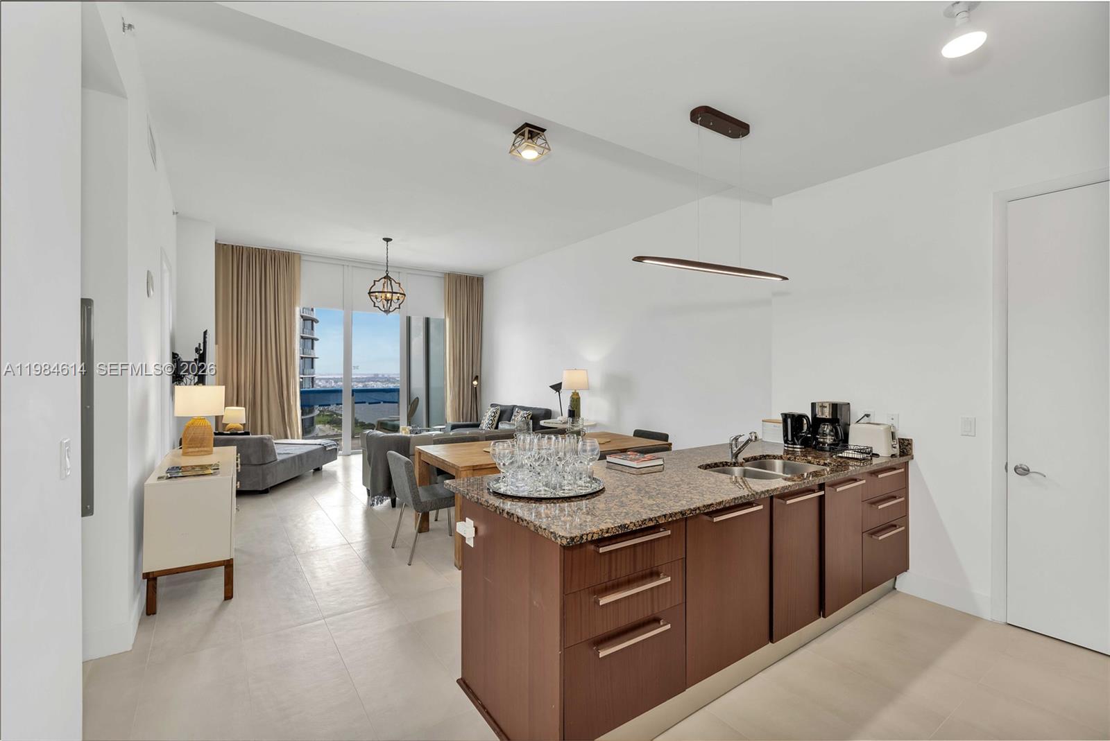 A modern kitchen island with granite countertops sits in an open-concept living and dining area — SUNNY ISLES BEACH, FL