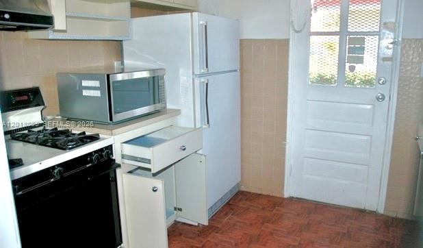 A kitchen features a white refrigerator, a microwave, a gas stove, and a tiled floor — MIAMI, FL