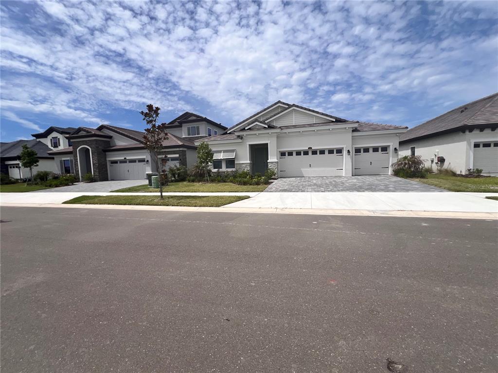 A single-story house with a three-car garage and a paved driveway under a cloudy sky — 9632 SURREY ROSE DRIVE, SAN ANTONIO, FL