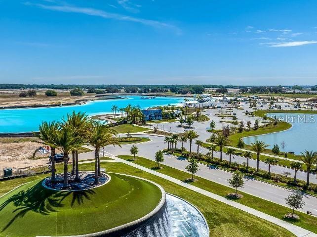 An aerial view shows a large turquoise lagoon surrounded by palm trees and paved parking — 9632 SURREY ROSE DRIVE, SAN ANTONIO, FL
