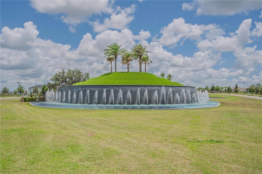 A large, circular fountain with a grassy mound and palm trees sits in a field — 9632 SURREY ROSE DRIVE, SAN ANTONIO, FL