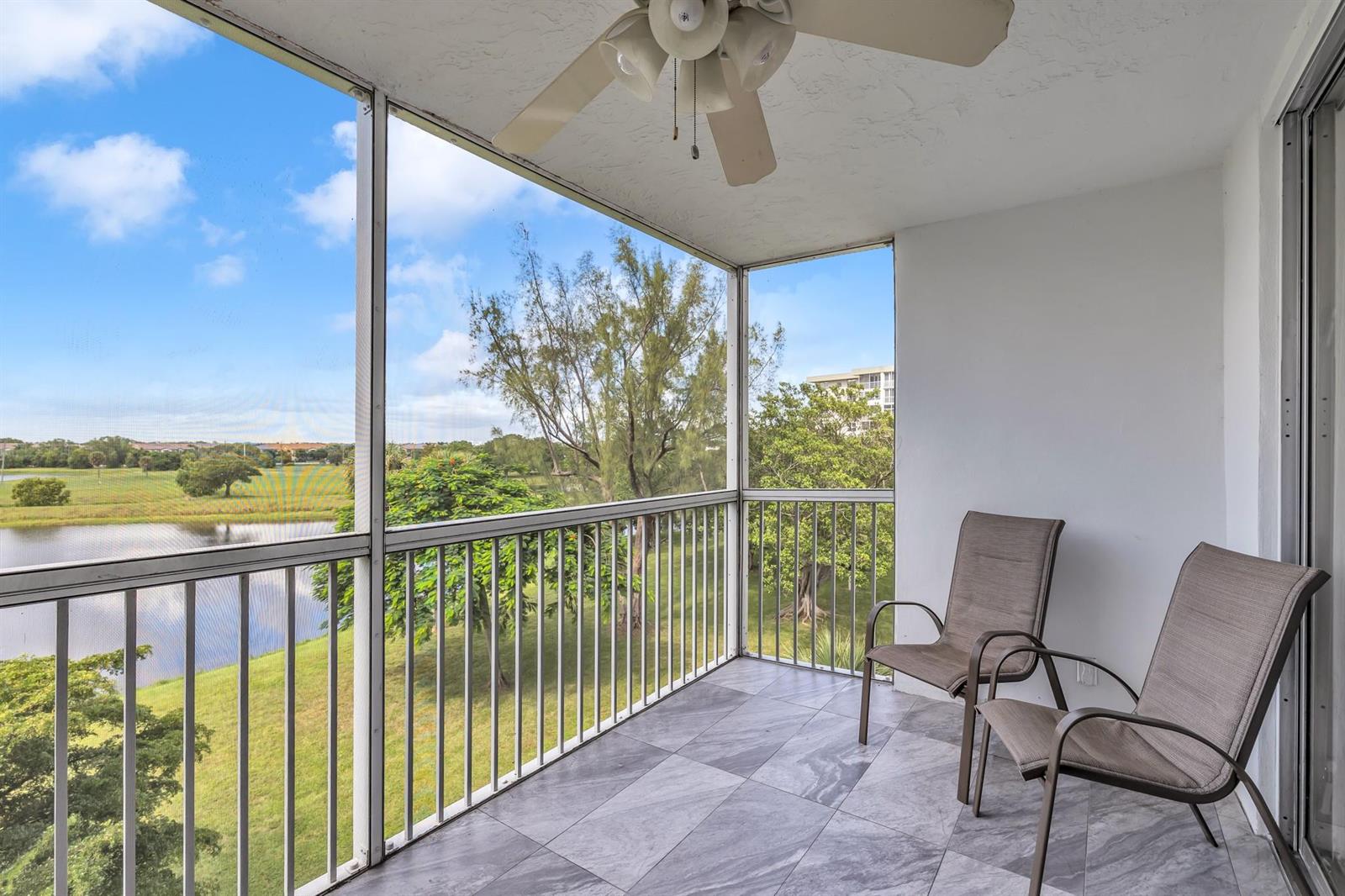 A screened-in balcony with gray tile flooring, two chairs, a ceiling fan, and lake views — 3080 N Course Drive # 501, Pompano Beach FL 33069, POMPANO BEACH, FL
