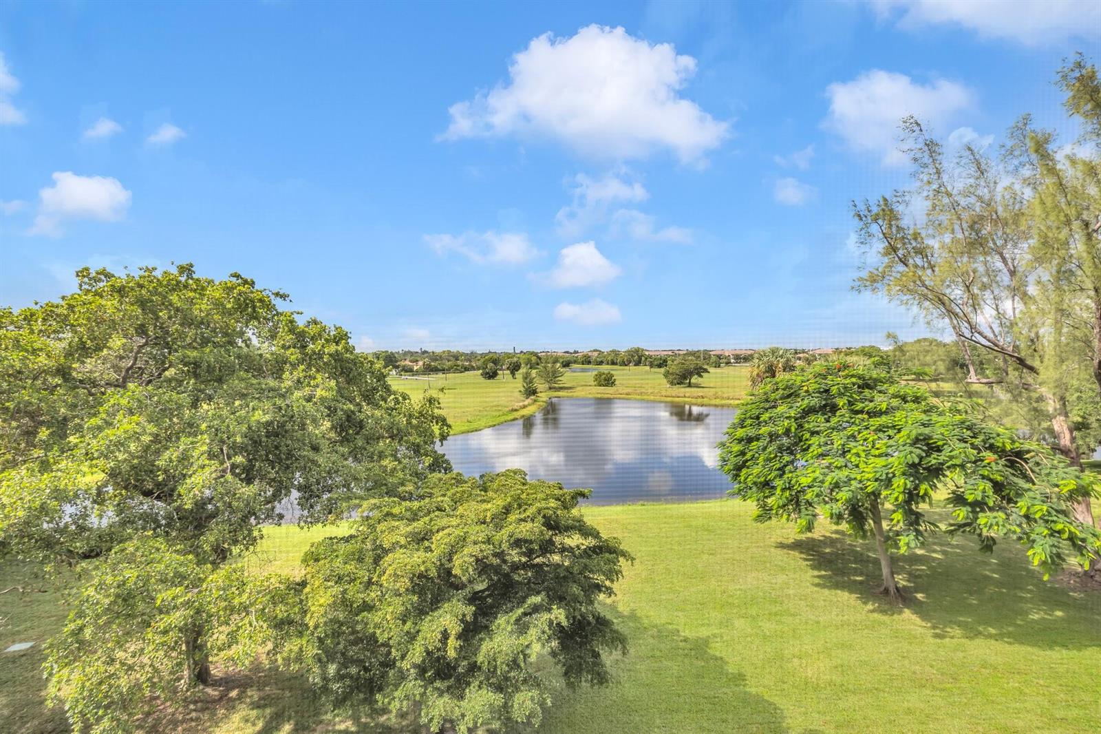 A view of a pond and green lawn surrounded by trees under a blue sky — 3080 N Course Drive # 501, Pompano Beach FL 33069, POMPANO BEACH, FL