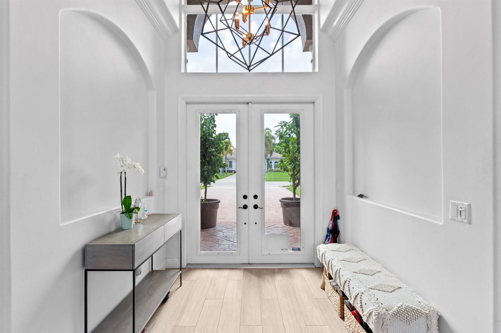 A bright entryway features white walls, arched alcoves, a modern chandelier, and a double door — 12442 Equine Lane, Wellington FL 33414, WELLINGTON, FL