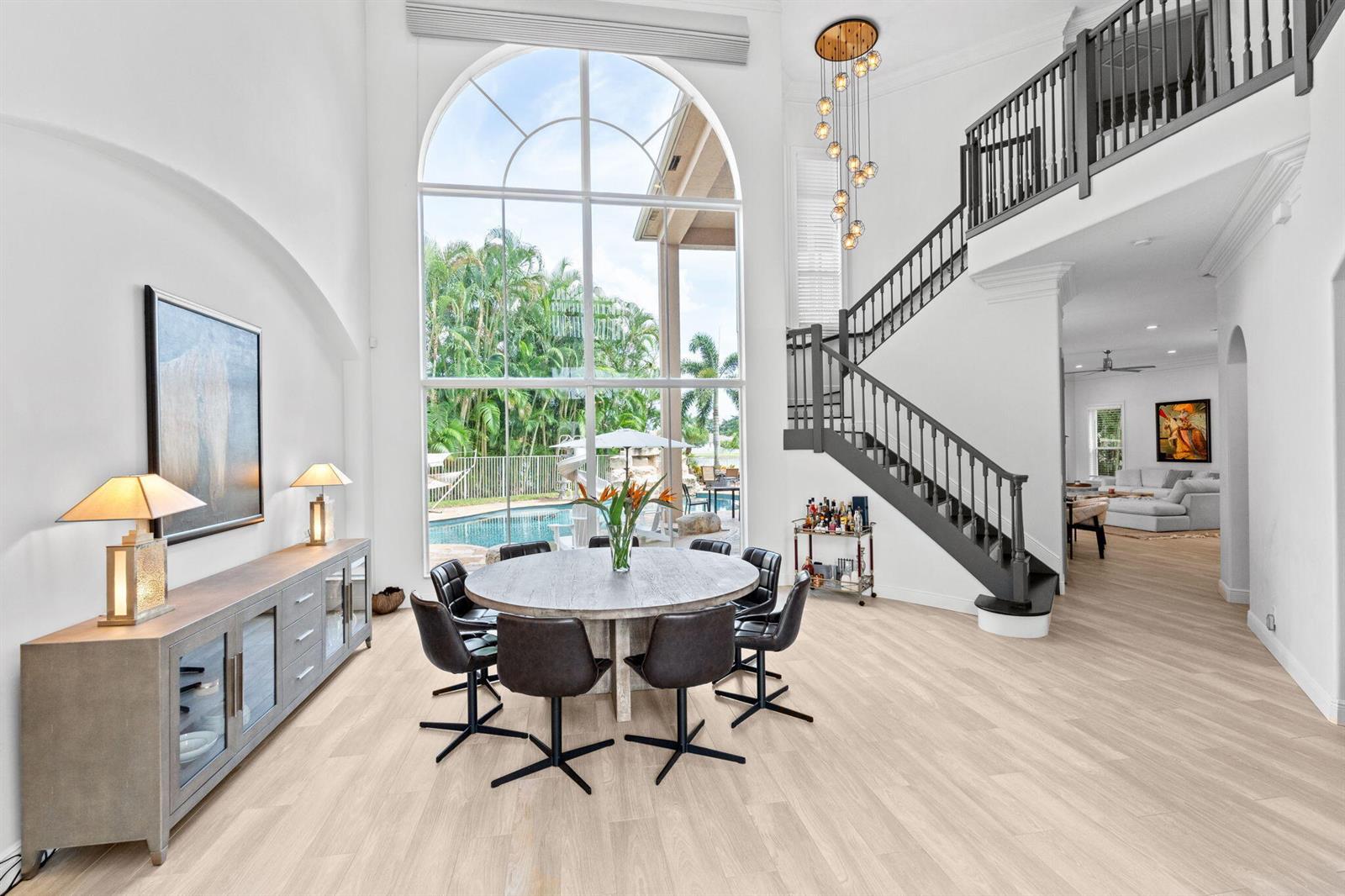 A dining area with a round table, dark chairs, and a large arched window overlooking a pool — 12442 Equine Lane, Wellington FL 33414, WELLINGTON, FL