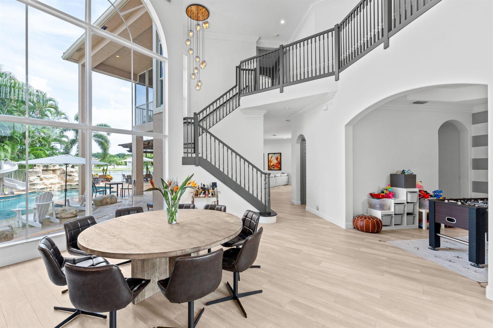 A dining area with a round wooden table sits beside a staircase and large windows — 12442 Equine Lane, Wellington FL 33414, WELLINGTON, FL