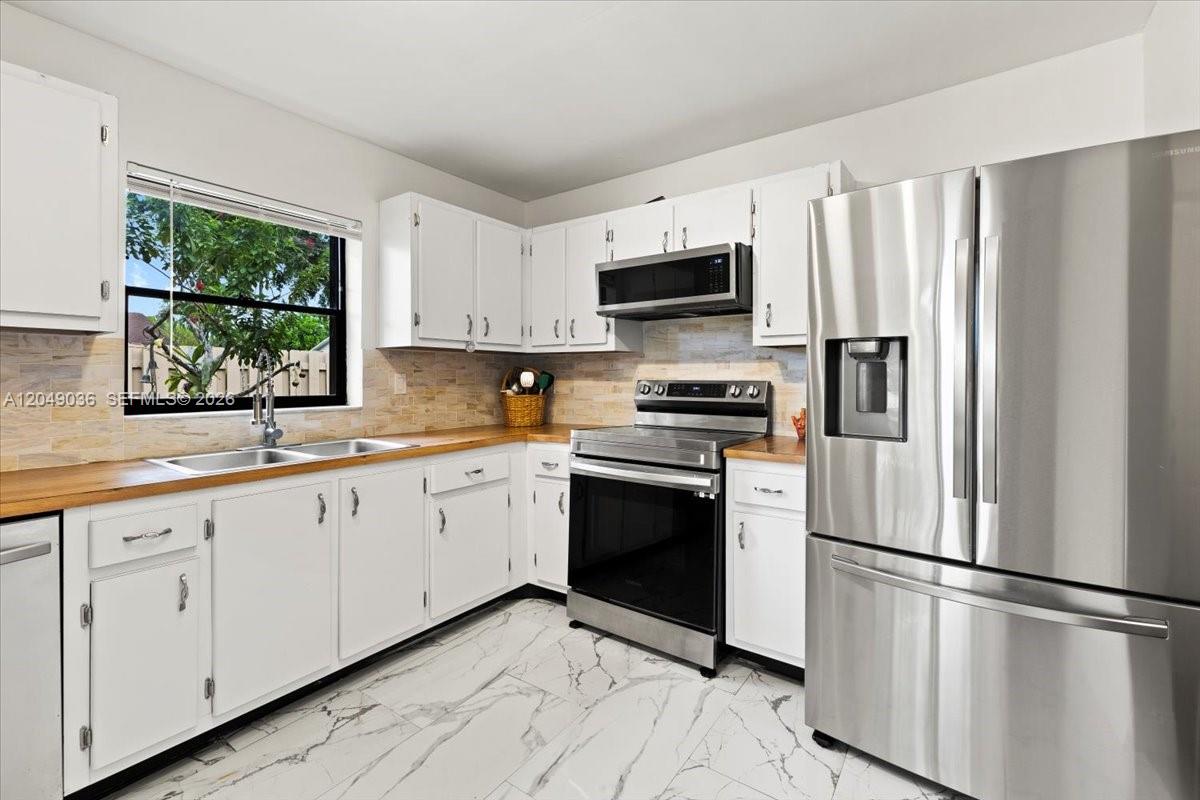 A kitchen features white cabinetry, stainless steel appliances, wood countertops, and white marble-patterned tile floors — 901 NW 26th Ave, Delray Beach FL 33445, DELRAY BEACH, FL